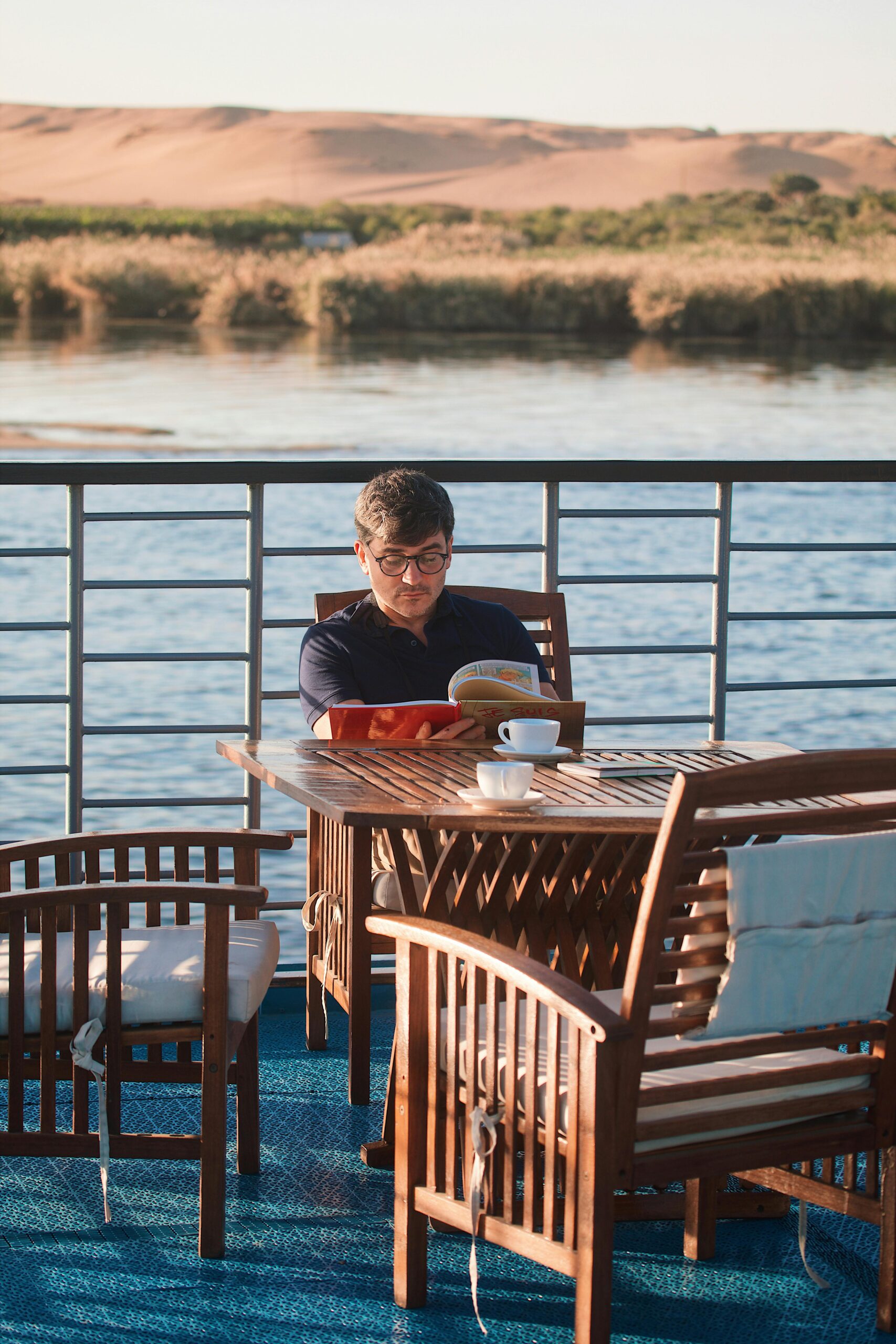 A man enjoys reading on a cruise deck overlooking the scenic Nile River in Egypt.